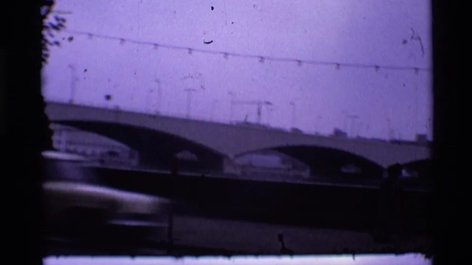 1969 London 8mm frame with a softly focused arched bridge, overhead lamps, and dark blurred street movement in front.
