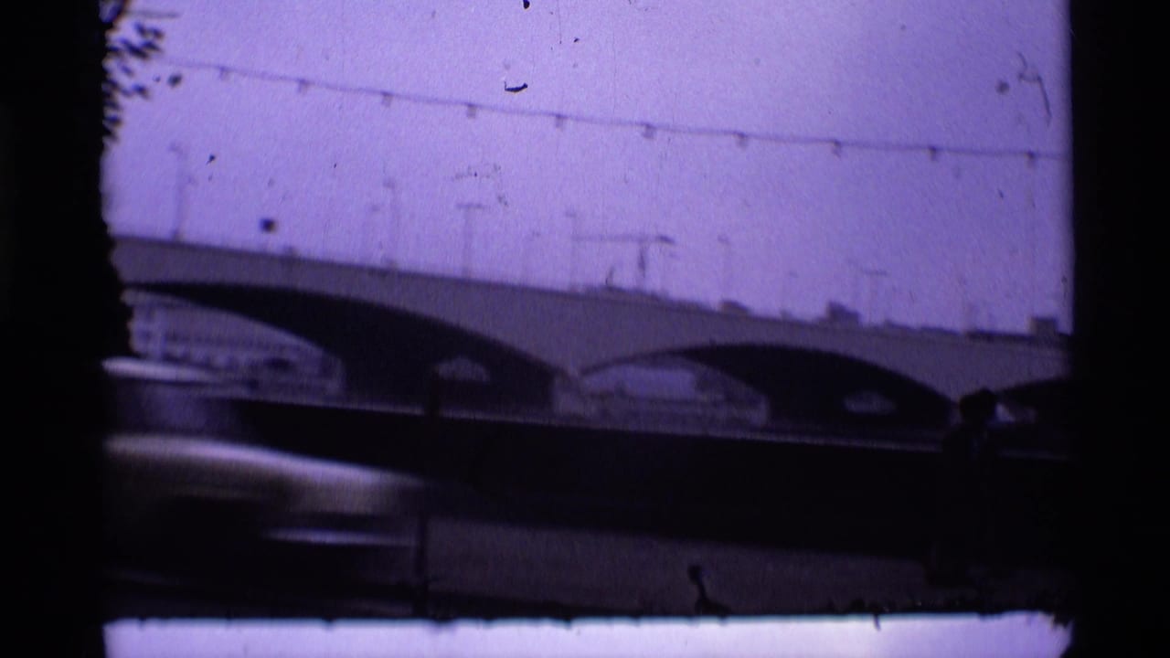 1969 London 8mm frame showing an arched bridge, pale purple sky, overhead wires, and a blurred car in the foreground.