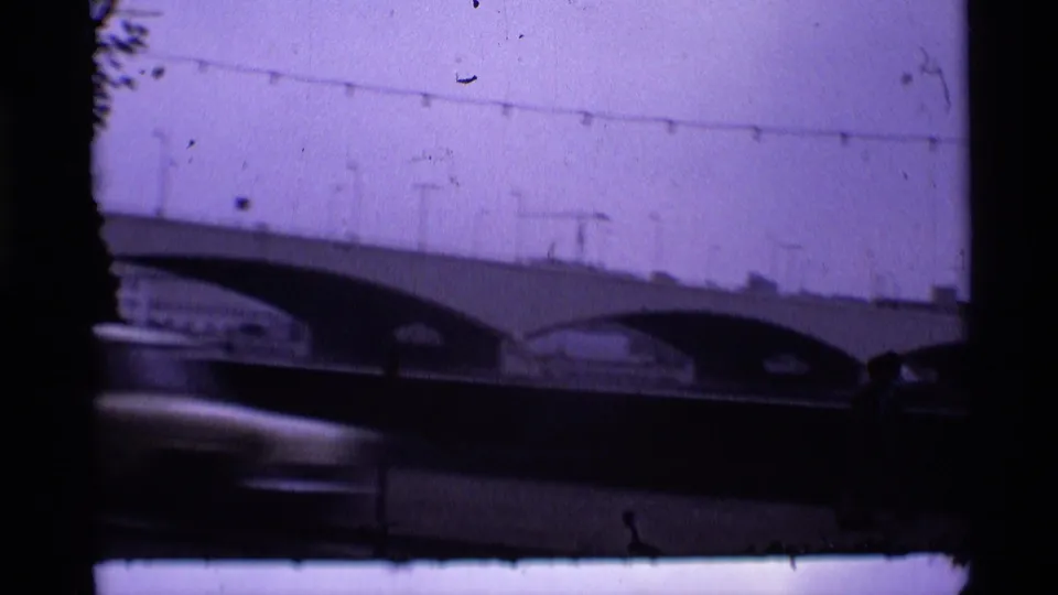 1969 London 8mm frame showing an arched bridge, pale purple sky, overhead wires, and a blurred car in the foreground.