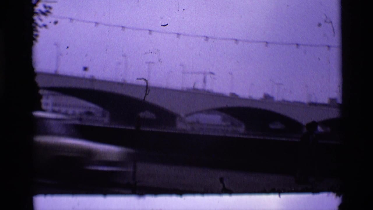 Arched bridge seen through a dark vehicle window with a car passing below.