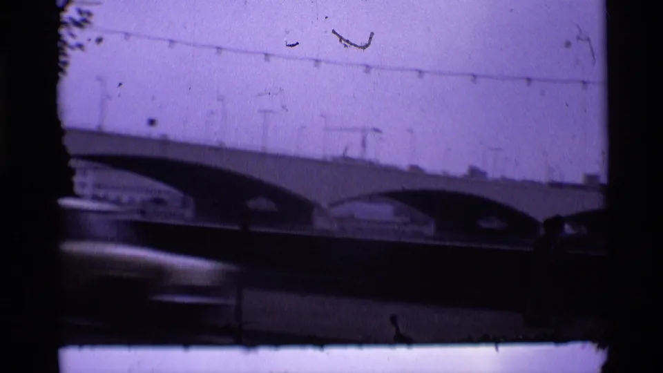 1969 London 8mm still with a large arched bridge over water, overhead wires, visible grain, and purple tint.