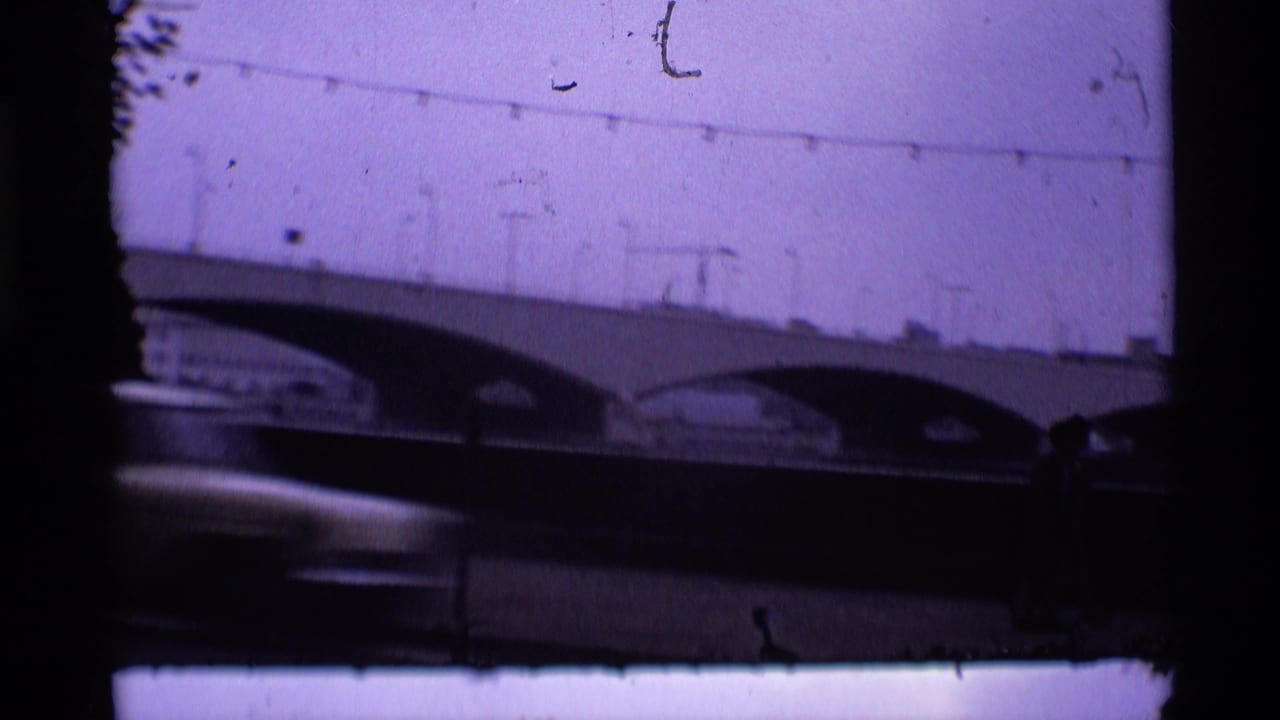 Arched bridge seen through dark film borders as a car blurs across the lower frame.