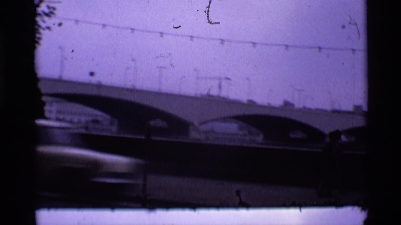 Concrete arched bridge over a dark roadway with blurred car movement and film scratches.