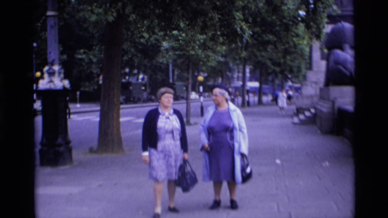 Two women walking together on a tree-lined city sidewalk.
