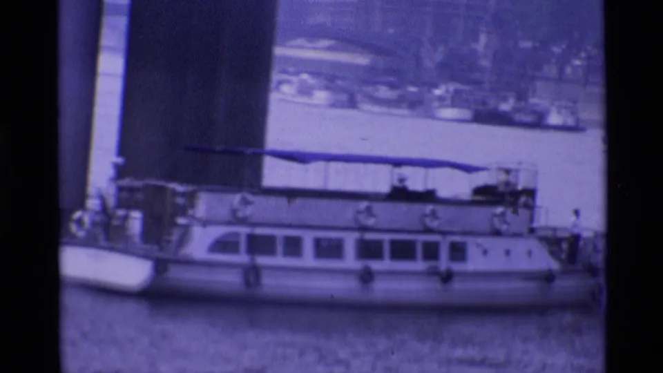 A river boat appears moored near a bridge or riverside structure, seen in soft focus with a purple-blue 8mm film cast.