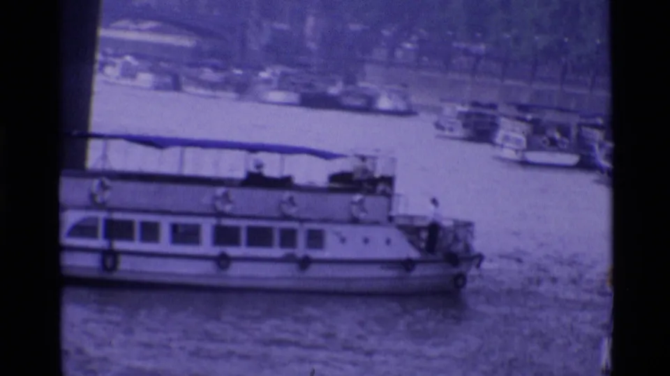 1969 London 8mm frame showing a large white riverboat passing near moored boats on the river.