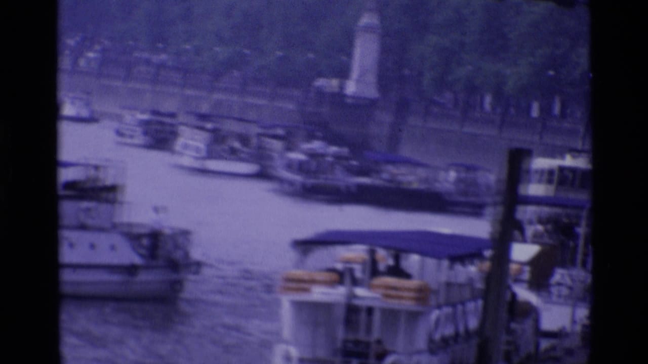 1969 London river view with boats, bridge structure, and small distant figures in a purple-tinted 8mm frame.