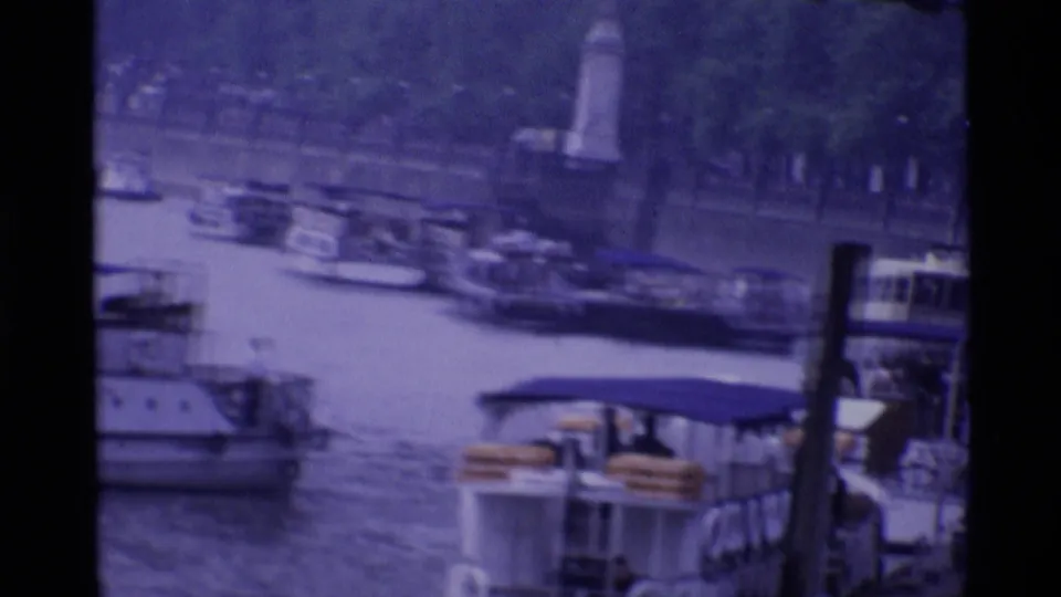 1969 London river view with boats, bridge structure, and small distant figures in a purple-tinted 8mm frame.