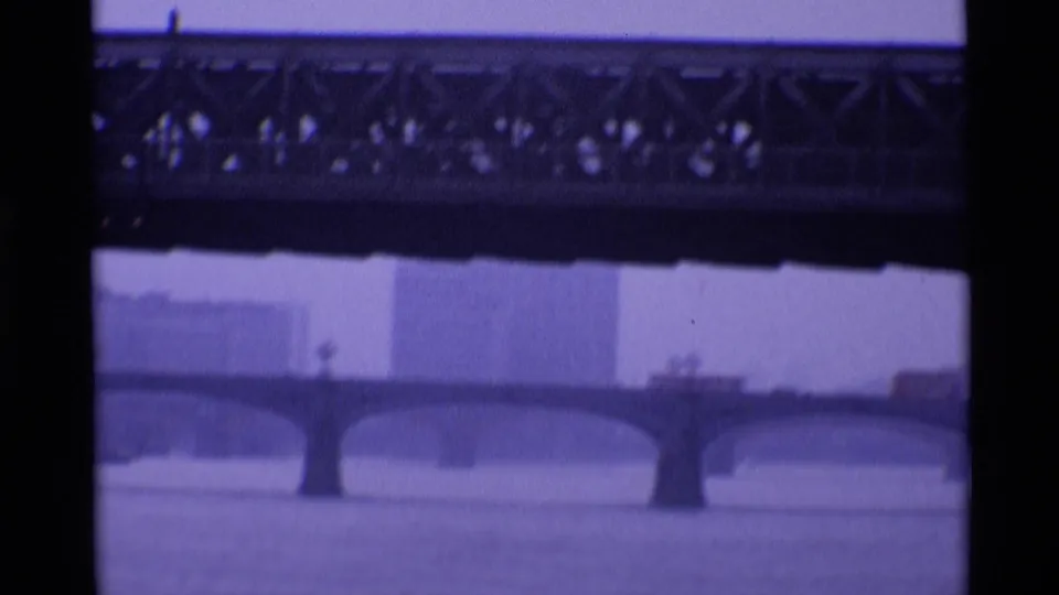 1969 London river frame with a stone arch bridge in the distance and dark trusswork across the foreground.