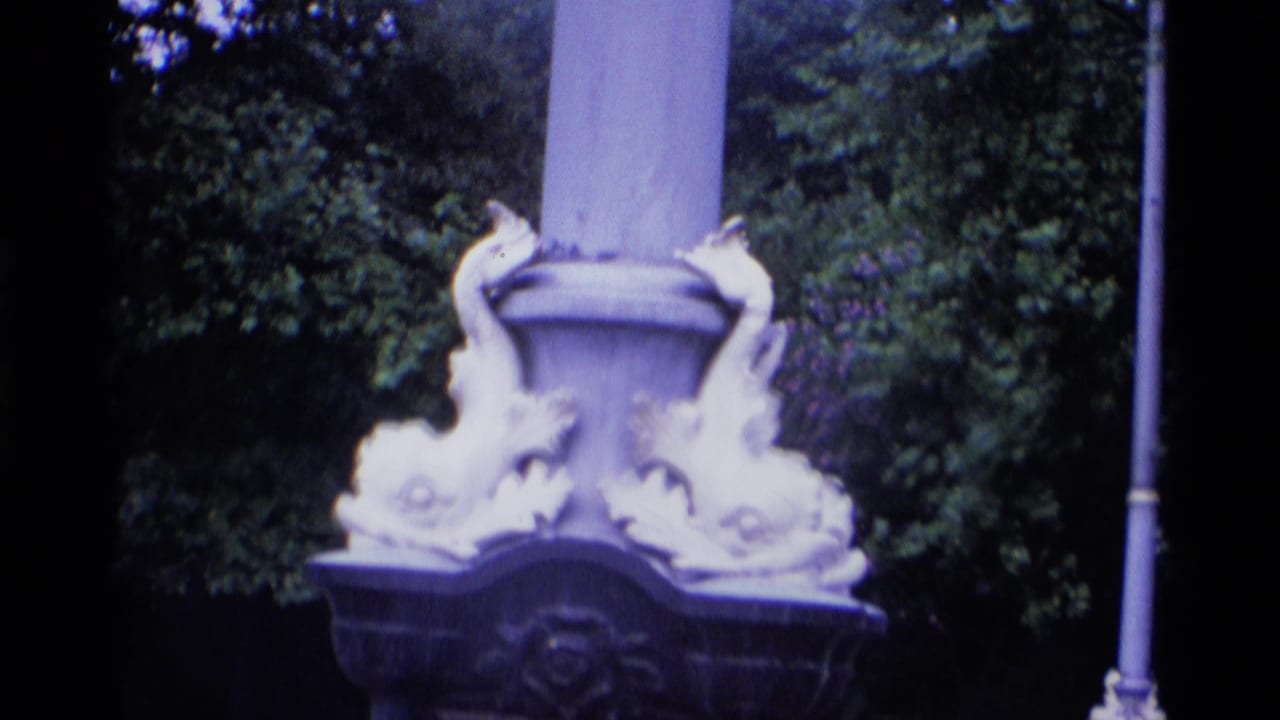 1969 London 8mm frame showing an ornate lamp base near dense trees and a roadside setting.