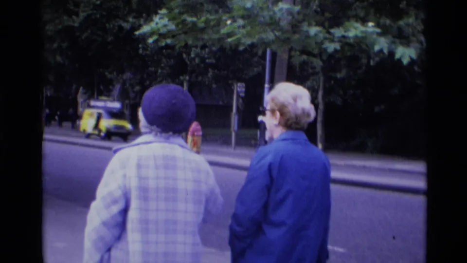 1969 London street view with two women walking away from the camera and a small car visible along the road.