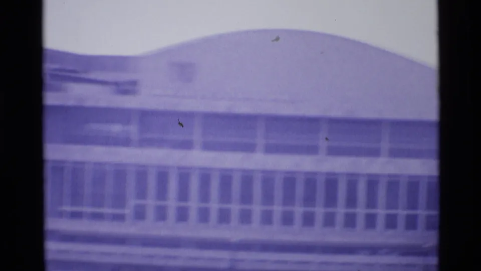 1969 London home-movie view of a broad curved-roof building with a long grid of windows below.