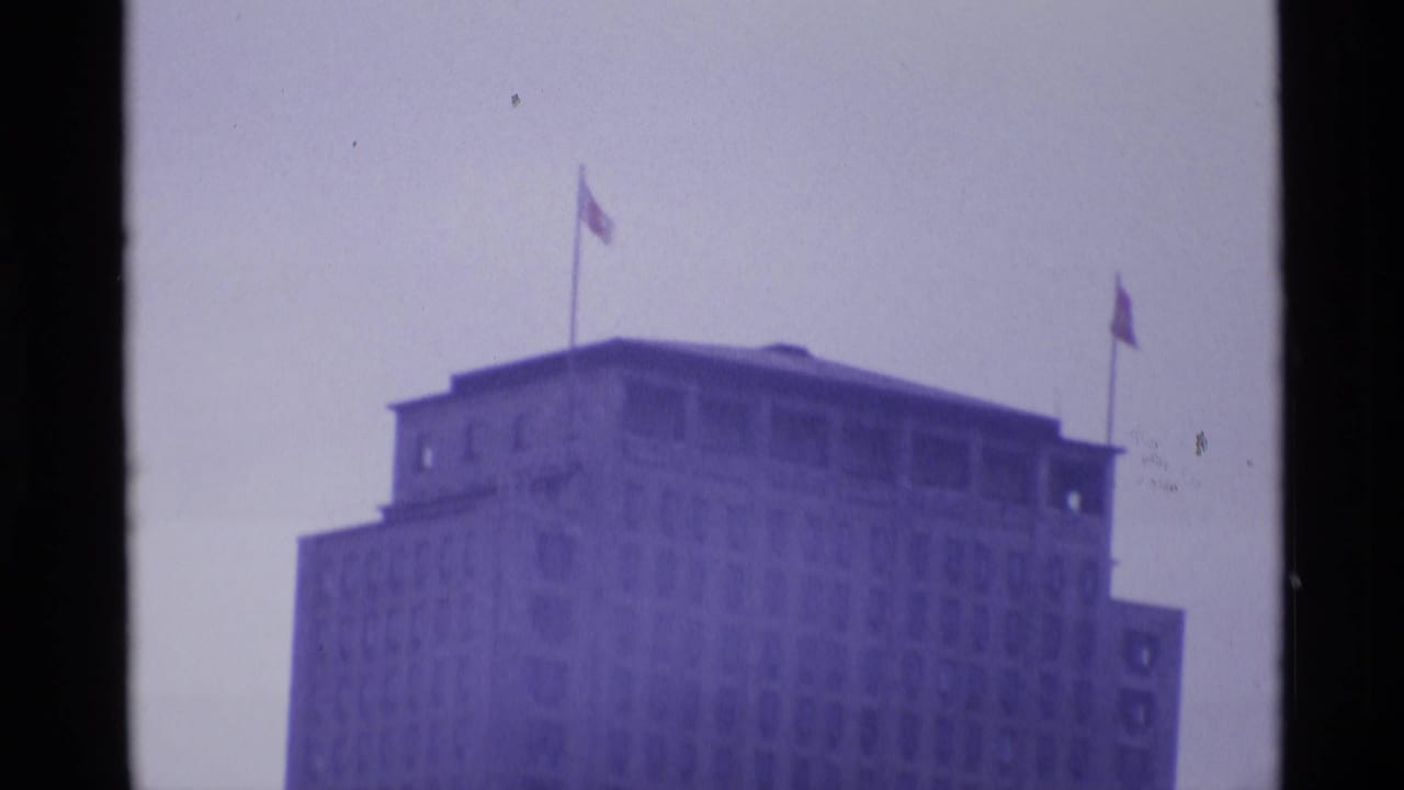 Tall windowed building with rooftop flags, filmed softly against a pale sky.