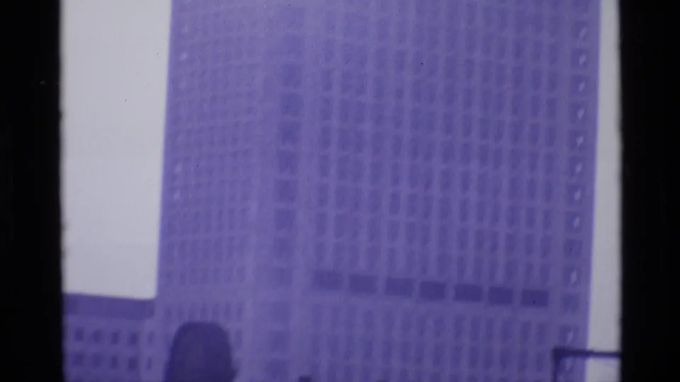 1969 London home-movie view of a large, windowed high-rise facade, softened by grain, exposure shift, and purple color cast.