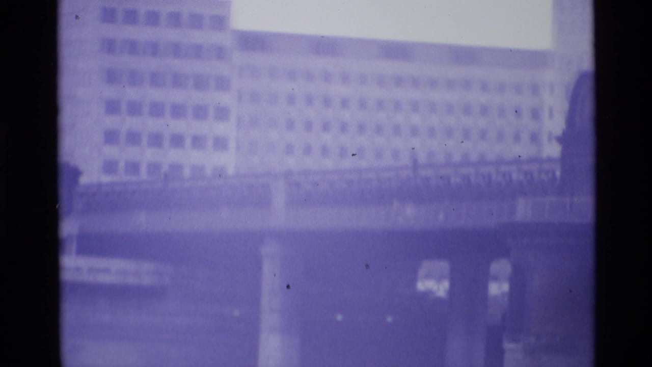 Soft purple-tinted view of a bridge deck with a large building behind it.