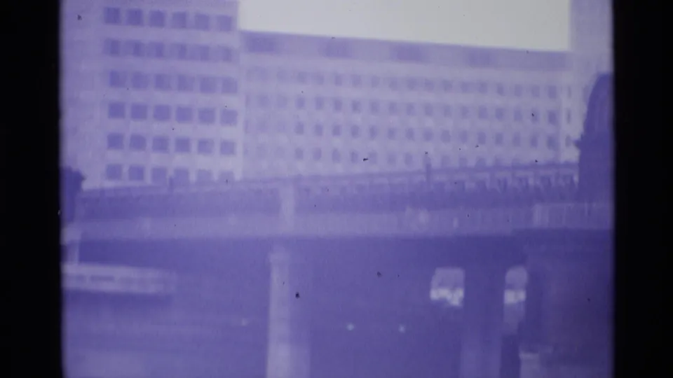 1969 London 8mm frame showing a long bridge section, concrete support, and large background building through soft purple film color.