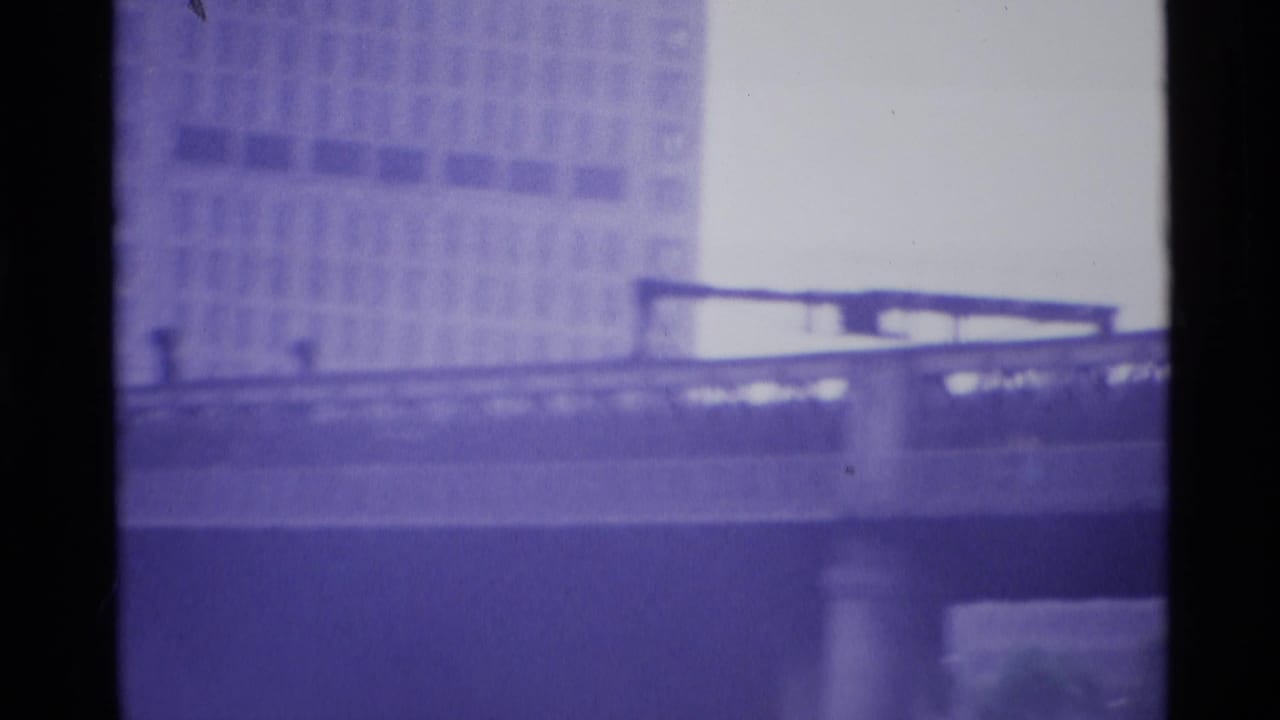 Moving 1969 London bridge view with a long railing, elevated deck, concrete support, and large building in the background.