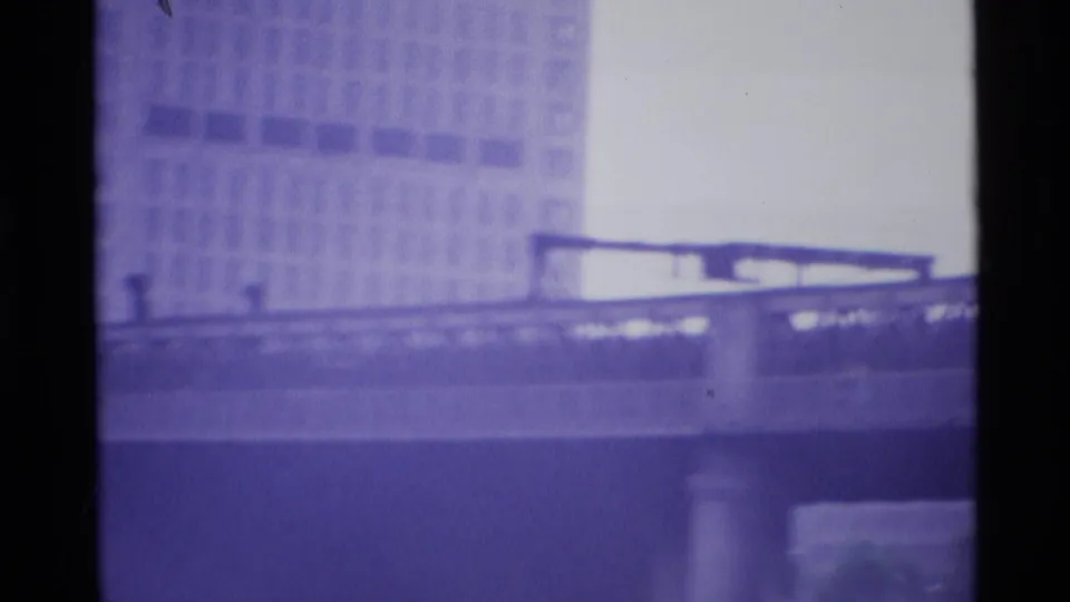 Moving 1969 London bridge view with a long railing, elevated deck, concrete support, and large building in the background.