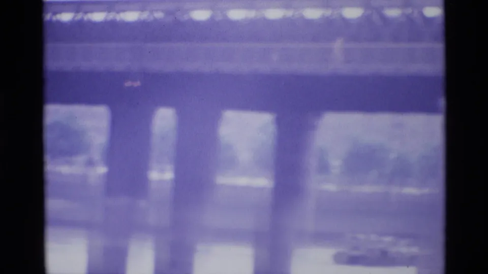 Purple-tinted 8mm view beneath a London bridge, with concrete piers, river surface, and blurred riverside details visible.