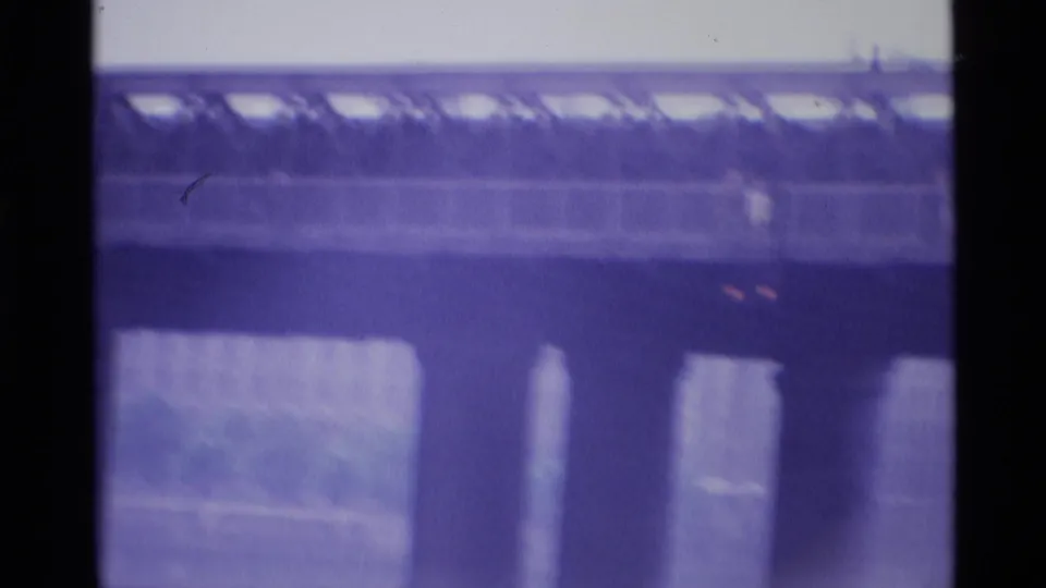 Final 1969 London 8mm frame showing a long bridge span, repeating supports, river below, and soft purple home-movie color.