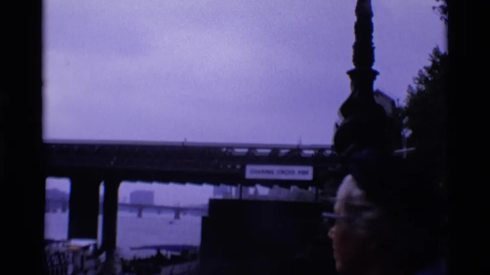 1969 London frame with a visible Charing Cross Pier sign, river and bridge beyond, and a partial face in the foreground.