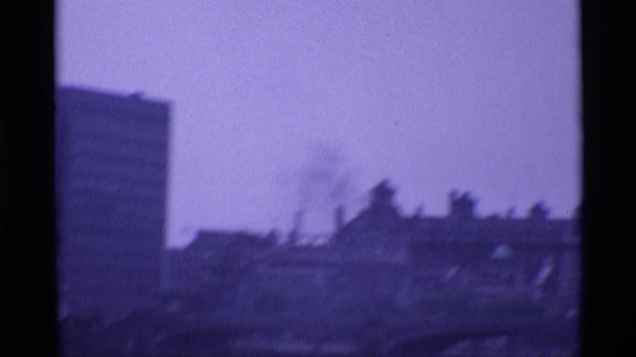 1969 London home-movie frame showing hazy riverside buildings, part of a bridge, and dark 8mm film borders.