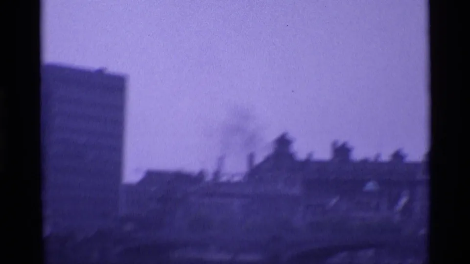 1969 London home-movie frame showing hazy riverside buildings, part of a bridge, and dark 8mm film borders.