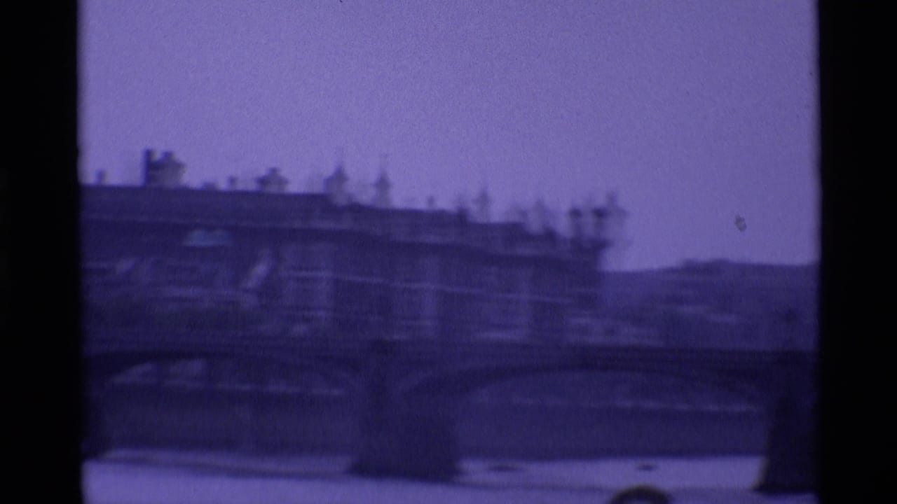 1969 London view of a multi-arch bridge over the river, with dense riverside buildings beyond in soft focus.