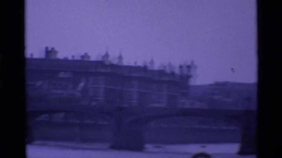1969 London view of a multi-arch bridge over the river, with dense riverside buildings beyond in soft focus.