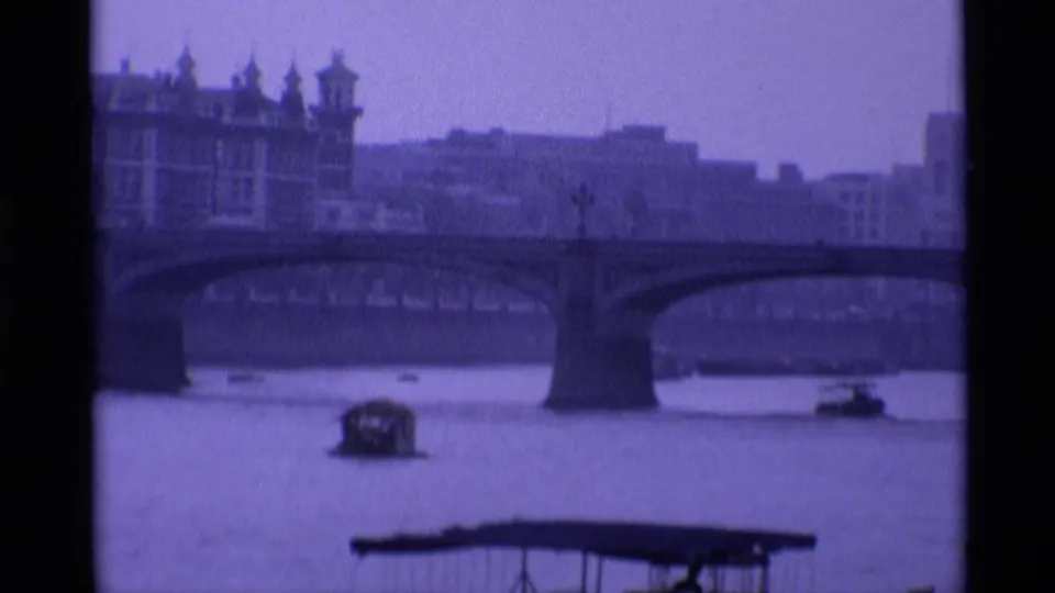 1969 London river view with a stone bridge, small boats passing below, and a large riverside building at left.