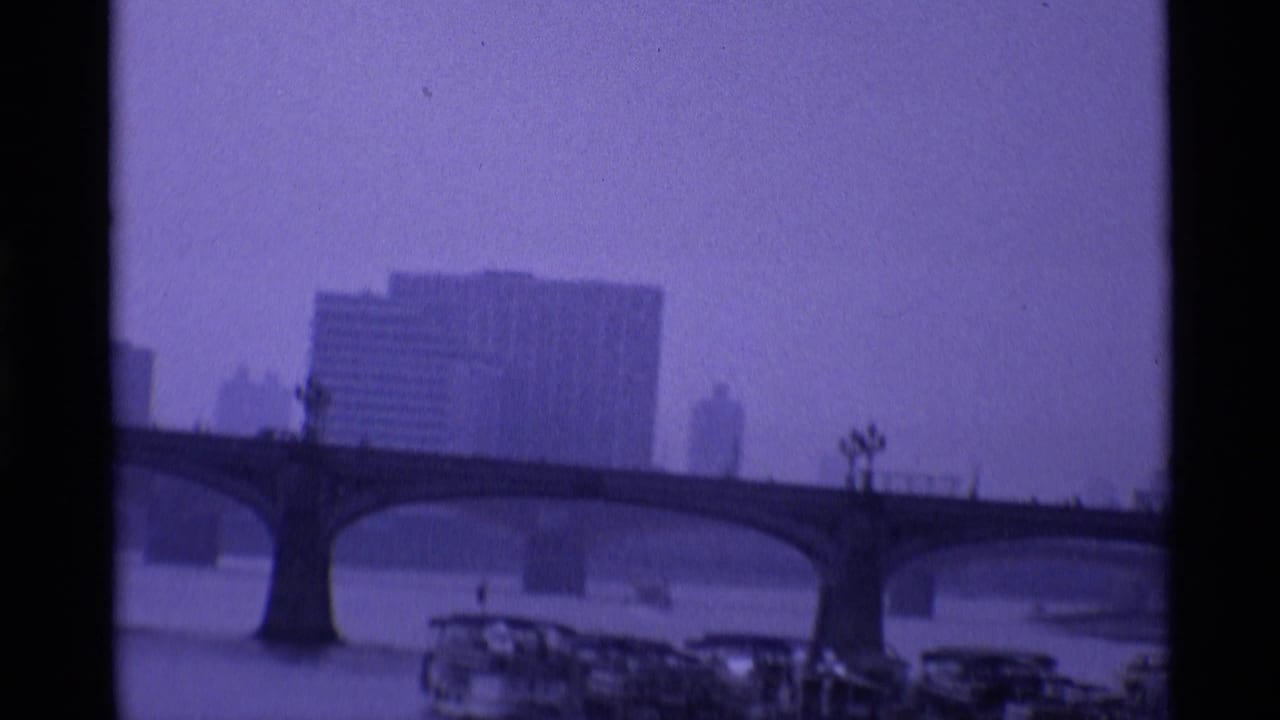 1969 London frame with an arched Thames bridge, boats near the riverbank and large buildings softened by dusk haze.