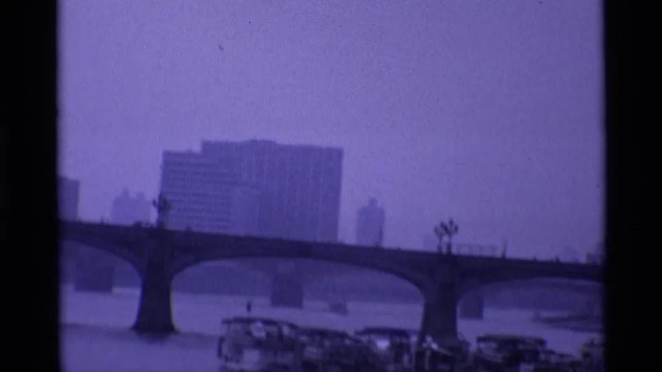 1969 London frame with an arched Thames bridge, boats near the riverbank and large buildings softened by dusk haze.