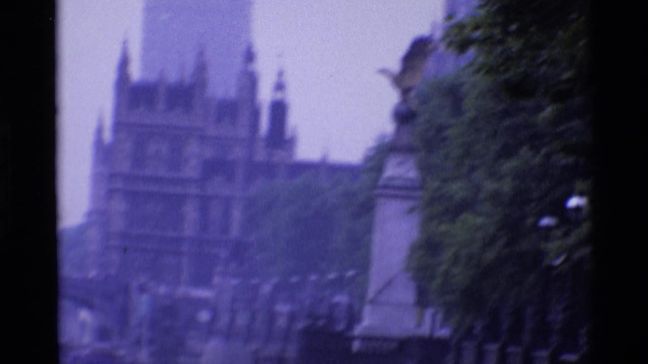1969 London 8mm frame showing a soft, distant view of pale ornate buildings and tower shapes partly screened by trees.