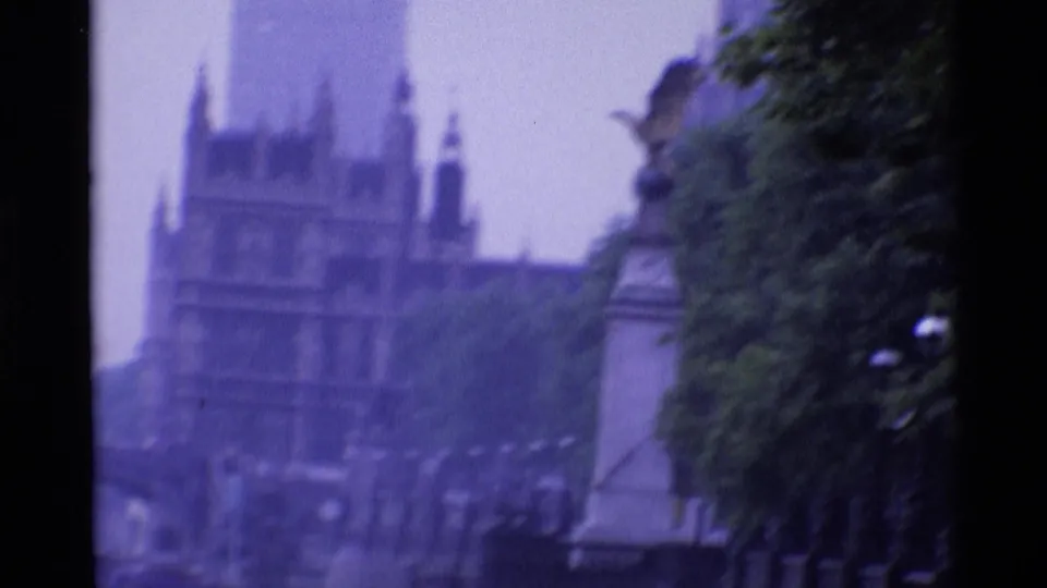 1969 London 8mm frame showing a soft, distant view of pale ornate buildings and tower shapes partly screened by trees.