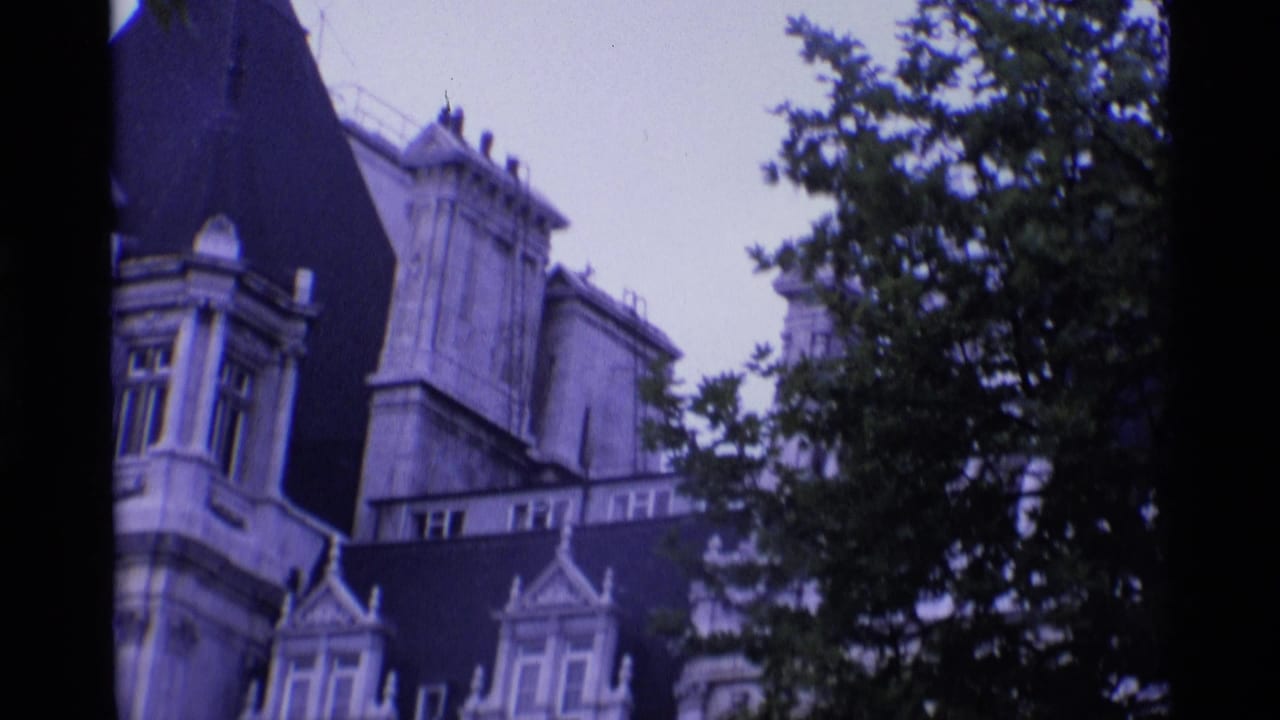 1969 London home-movie frame showing ornate stone buildings with arched windows partly obscured by a leafy tree.