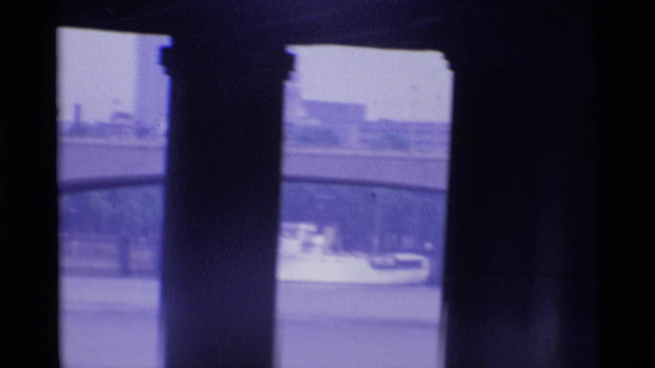 London river scene viewed through dark pillars, with embankment details and a light-colored boat in the distance.