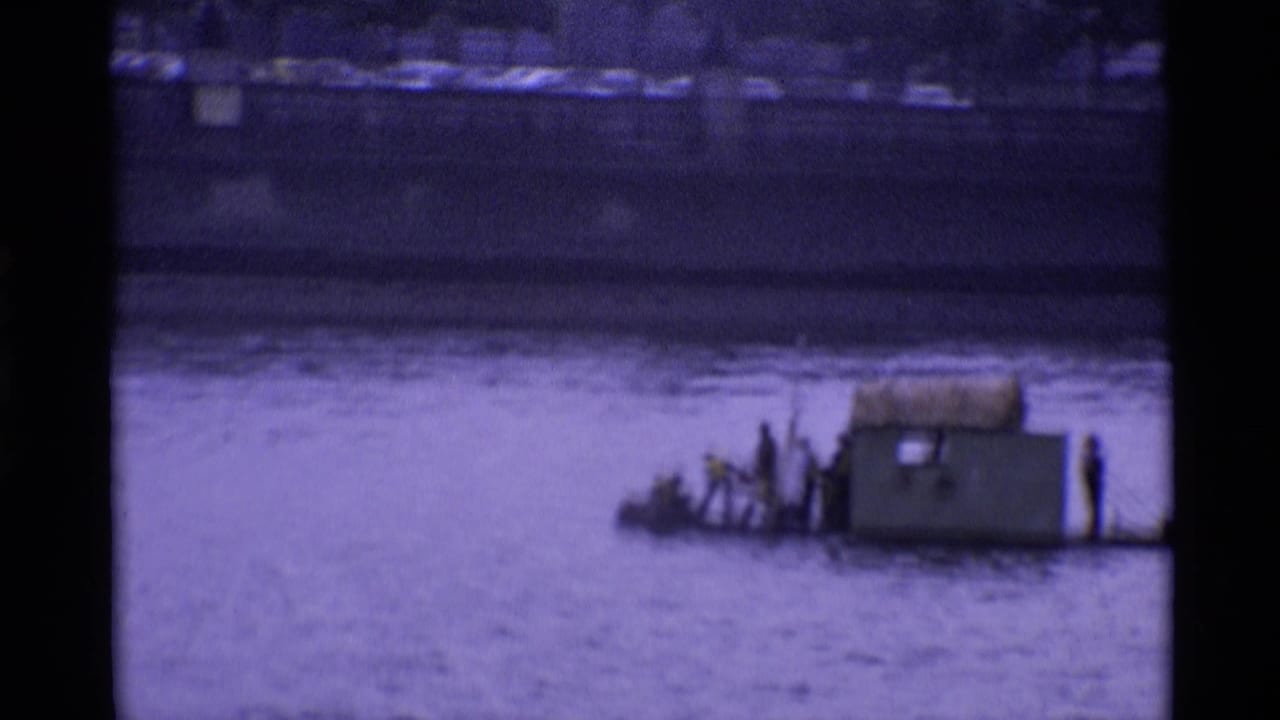 1969 London 8mm frame showing men on a low makeshift river craft with a small cabin-like structure.