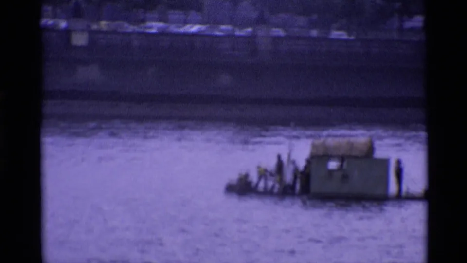 1969 London 8mm frame showing men on a low makeshift river craft with a small cabin-like structure.