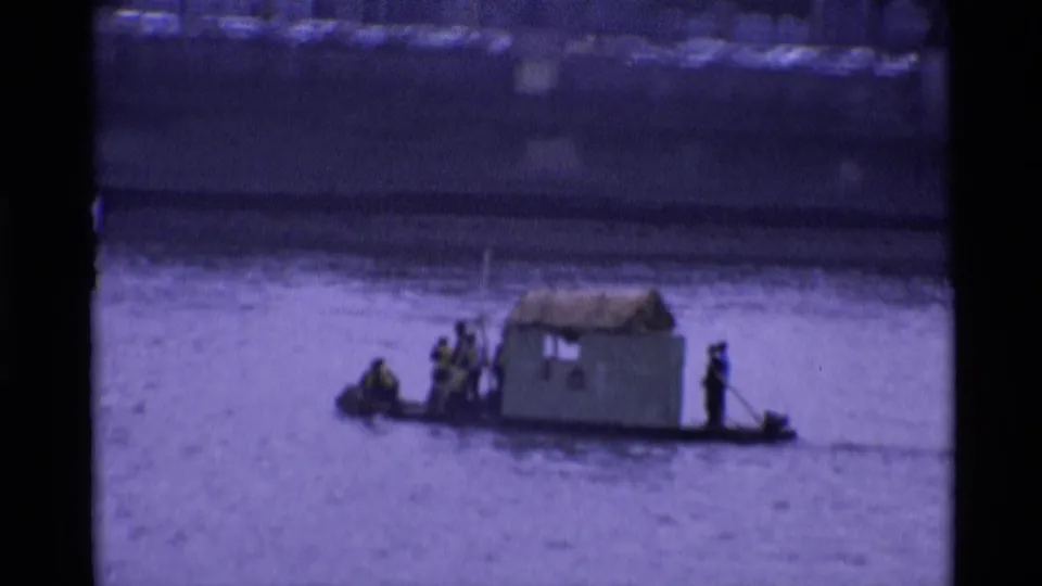 Soft 8mm 1969 London frame showing men on a makeshift river boat with a hut-like center shelter.