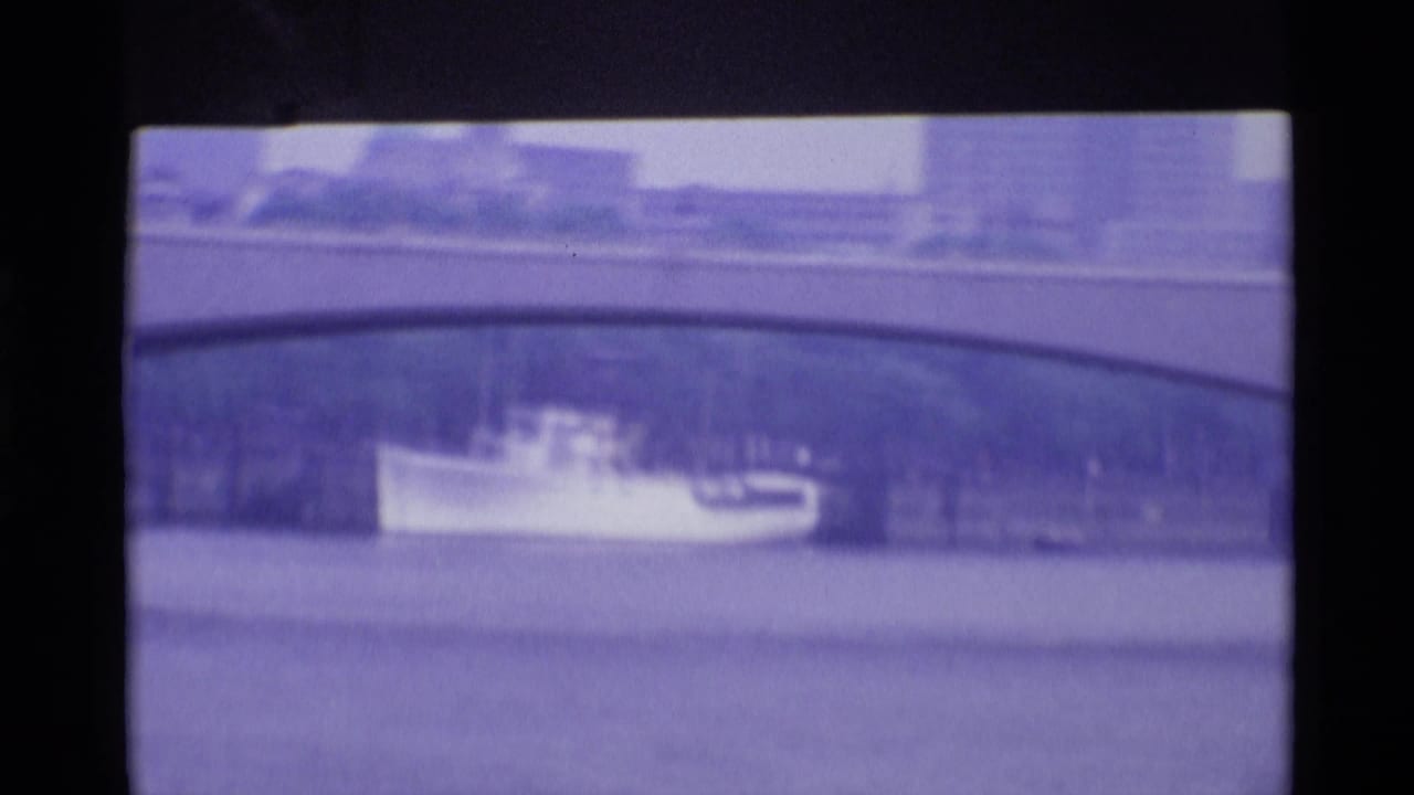 1969 London river view with a small boat passing beneath or near a stone bridge, framed by distant waterfront buildings.