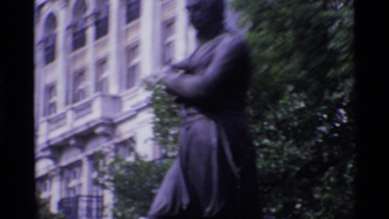 1969 London 8mm frame showing a dark public statue near leafy trees and a pale, ornate building facade.