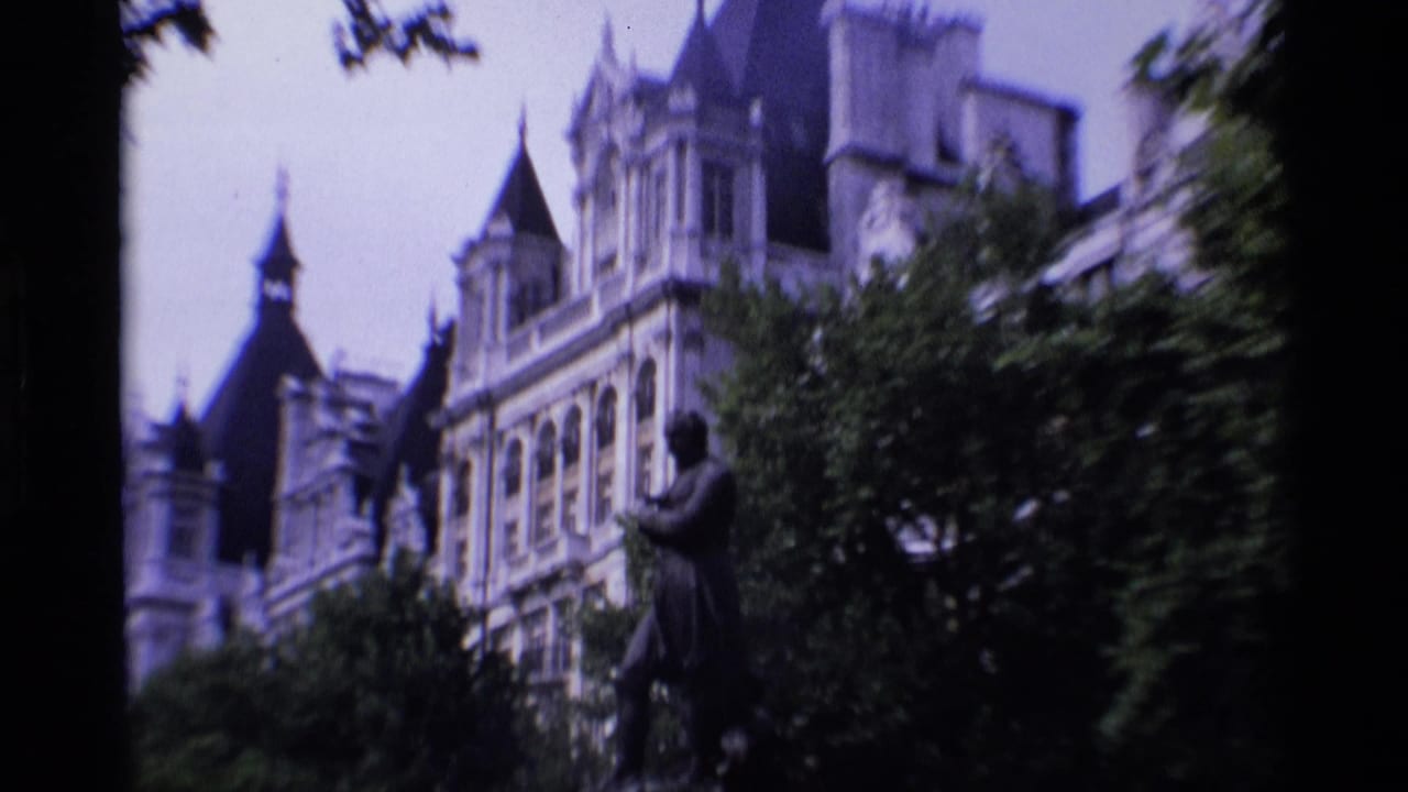 1969 London 8mm frame with a statue and leafy trees before an ornate stone building with spires and steep rooflines.