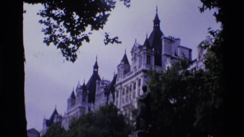 1969 London 8mm frame showing ornate spired architecture and a statue partly obscured by tree branches.