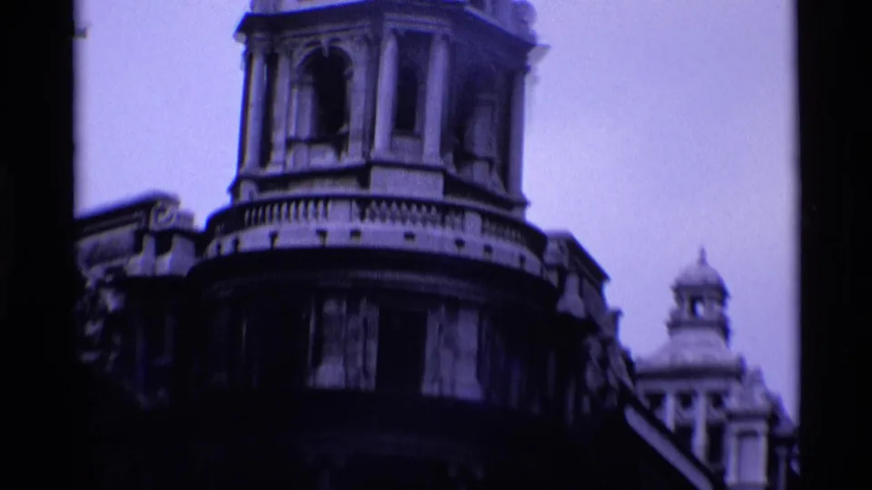 1969 London 8mm frame of a grand rounded stone building corner with tower windows, balustrade detail, and a smaller dome in the distance.