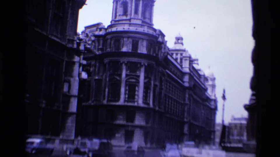 1969 London 8mm frame showing a wider street view of an ornate stone building, with cars at street level and soft handheld framing.