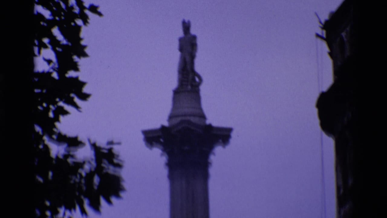 Soft 1969 London home-movie view of Nelson's Column framed by dark tree branches and heavy purple color shift.