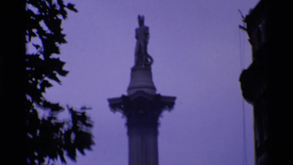 Soft 1969 London home-movie view of Nelson's Column framed by dark tree branches and heavy purple color shift.