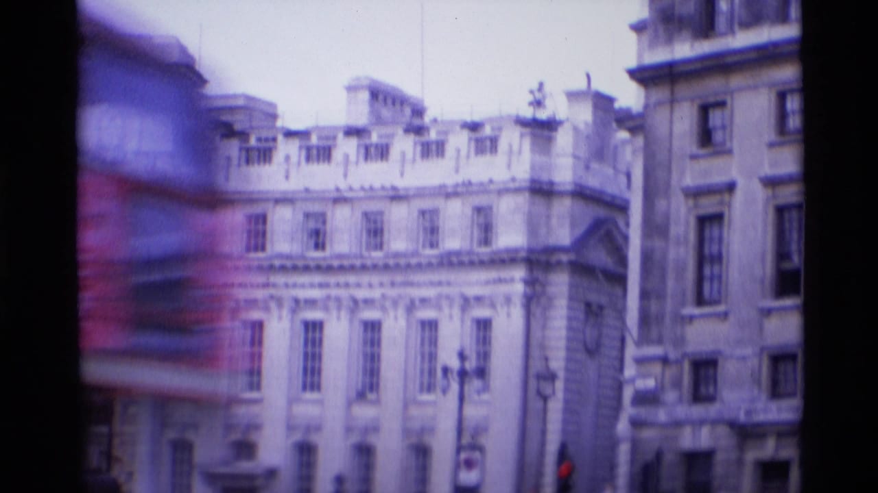 1969 London street view with a blurred red double-decker bus crossing historic stone building facades.