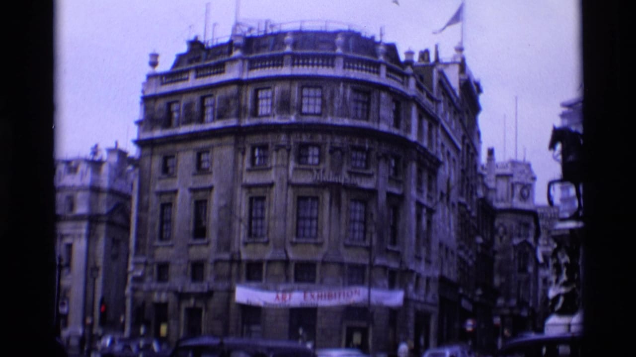 1969 London corner street scene showing a multi-story historic building, traffic, and a street-level banner.