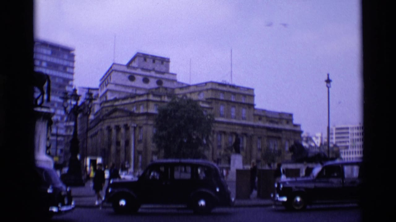 Black taxis and pedestrians pass near a large classical building.